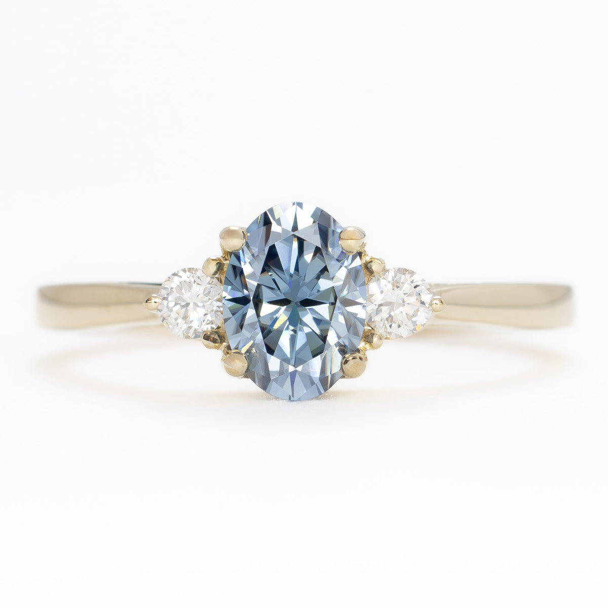 carina three stone ring in yellow gold with oval blue moissanite