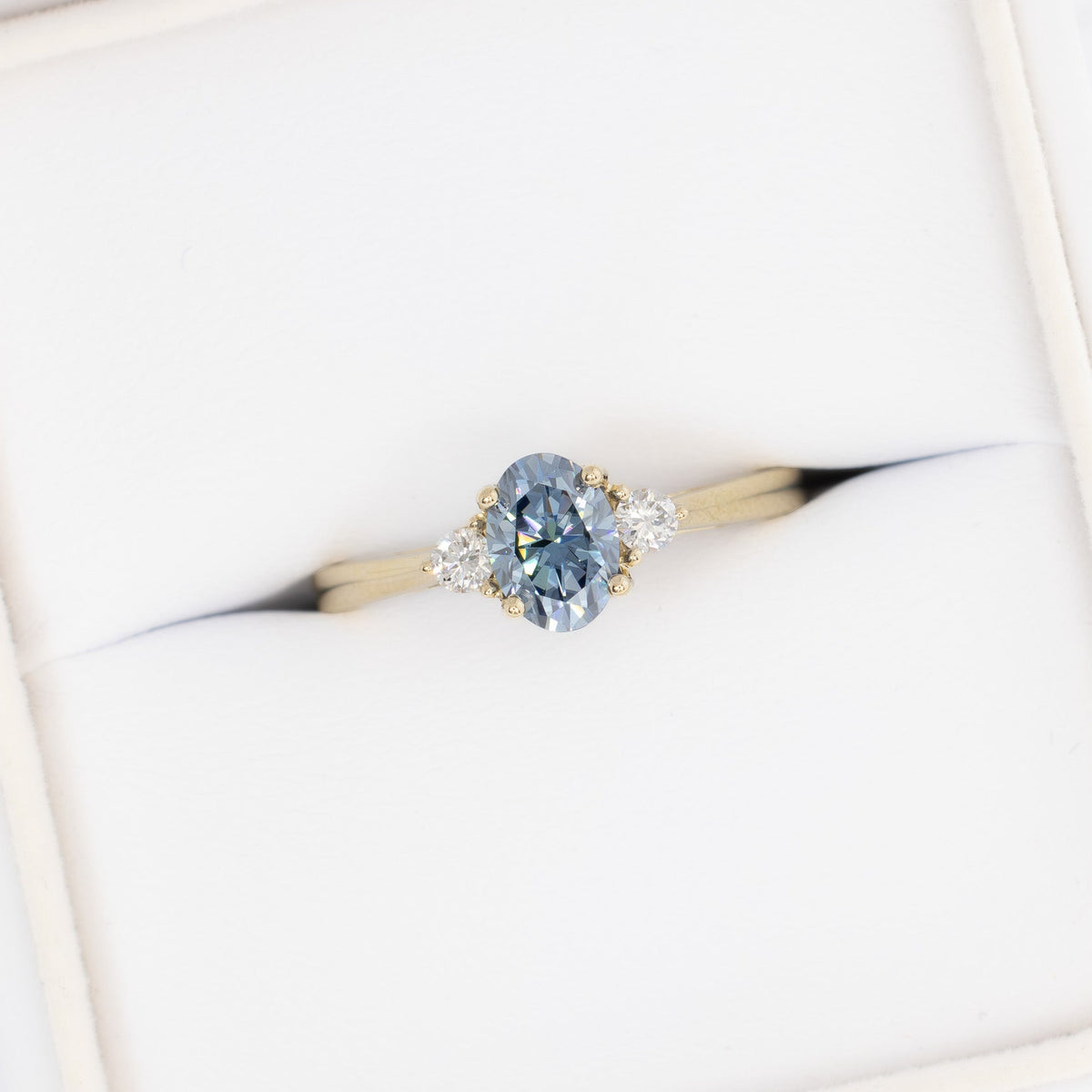 carina three stone ring in yellow gold with oval blue moissanite